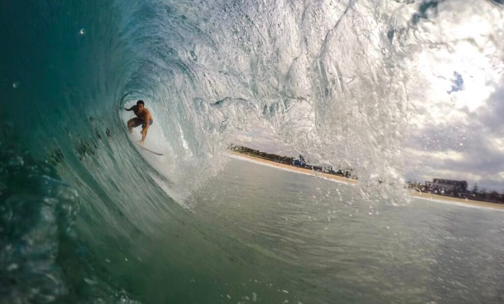 Surfer inside a breaking barrel looking out toward the beach